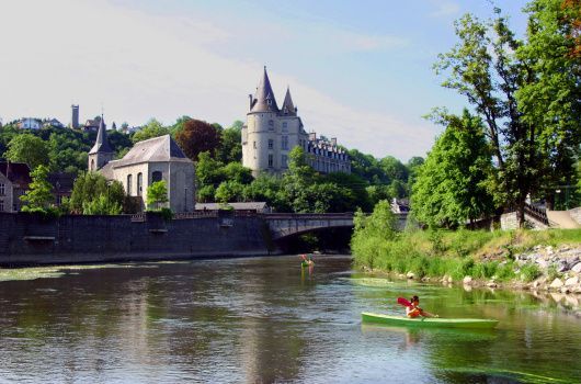 Kayaks sur l’Ourthe avec maisons en pierre et clocher en arrière-plan